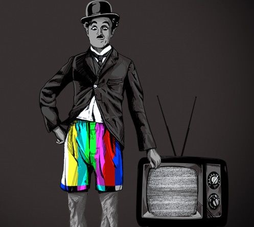 Charlie Chaplin está ao lado de uma televisão antiga , com um chapeu e um terno na parte de cima do corpo e embaixo está com uma bermuda colorida, remetendo a uma tv com canais coloridos.